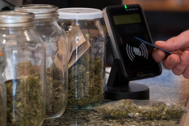 A person purchasing jars of marijuana flower with a credit card at a dispensary.