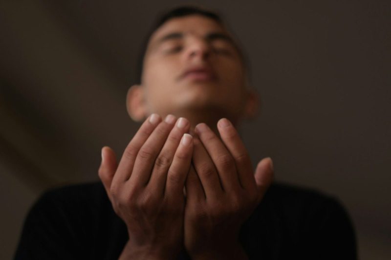 Young man with hands clasped and eyes closed.
