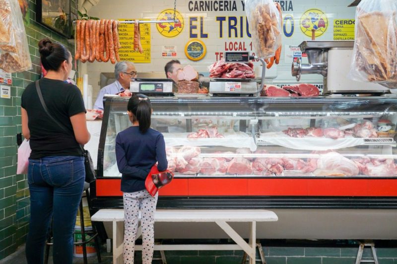 Mexico City, Mexico - October 14 2019 - A woman and a child at a carniceria, which is a meat counter, with lots of different meats on display at a market in the suburb of San Angel, Mexico City.