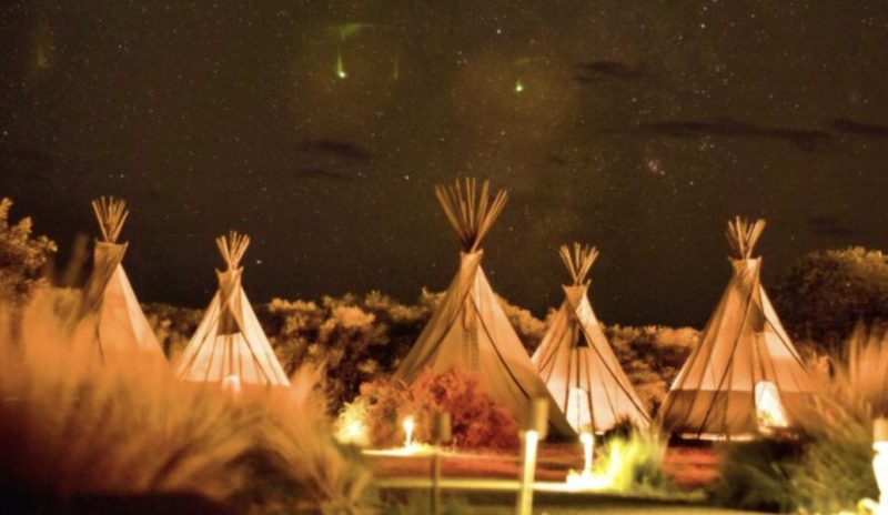 A glamping tipi site at nighttime illuminated by torches and the stars.